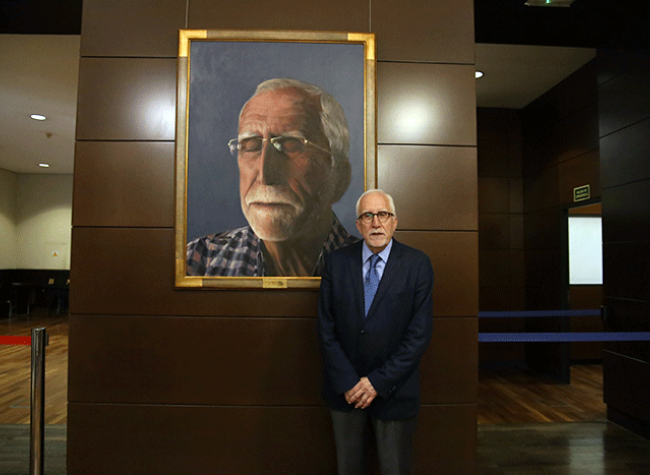 Luis Mateo Díez posa junto al retrato de Jorge Diezma